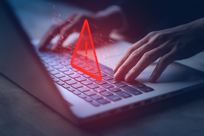 a laptop with a red warning sign highlighting the dangers that arise from phishing scams