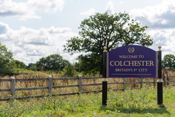 A welcome to Colchester sign next to a country field